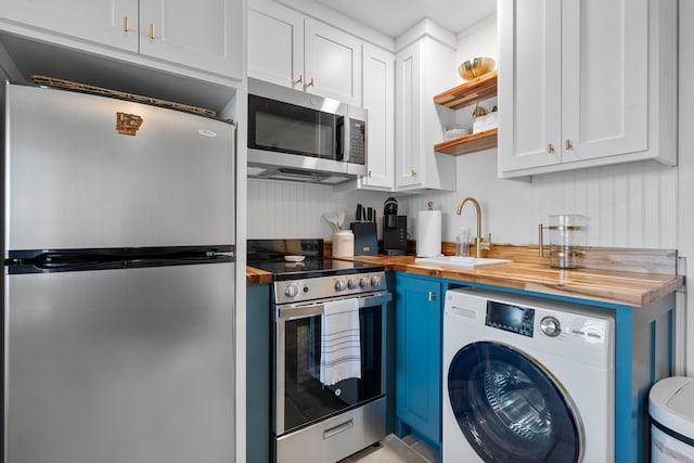 kitchen featuring a sink, open shelves, washer / clothes dryer, stainless steel appliances, and wooden counters