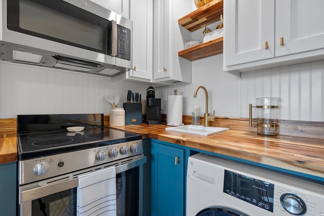 kitchen featuring washer / dryer, blue cabinetry, a sink, appliances with stainless steel finishes, and wood counters