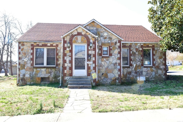 view of front of property with entry steps, a front lawn, and roof with shingles