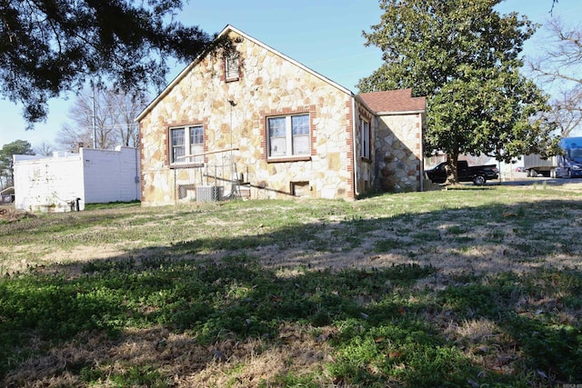 view of side of property with a yard, stone siding, and central AC