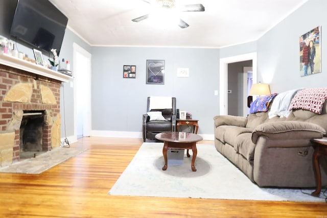 living room with baseboards, ceiling fan, ornamental molding, a fireplace, and wood finished floors