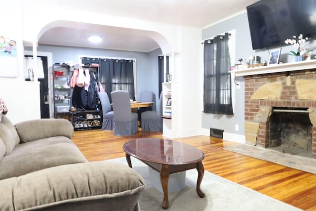 living area with a brick fireplace, wood finished floors, arched walkways, and baseboards