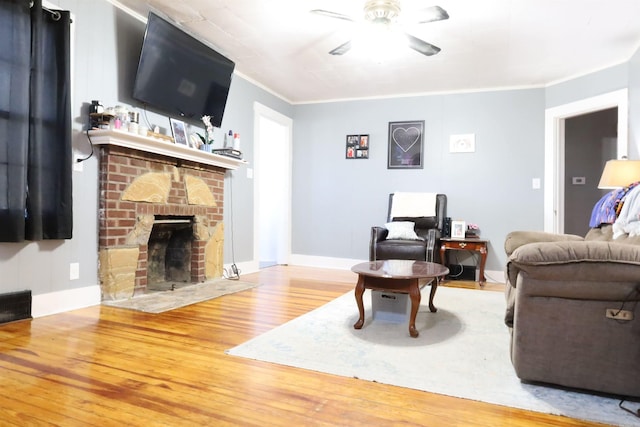 living area featuring a brick fireplace, baseboards, ceiling fan, ornamental molding, and wood finished floors