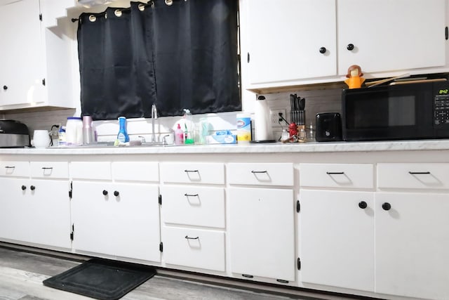 kitchen featuring white cabinetry, light countertops, black microwave, and a sink