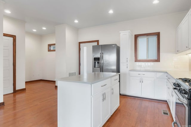 kitchen featuring visible vents, light wood-style flooring, tasteful backsplash, a center island, and stainless steel appliances