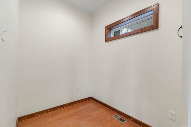 empty room featuring visible vents, light wood-style flooring, baseboards, and ornamental molding