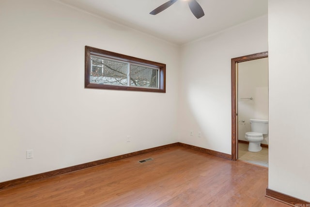 unfurnished bedroom featuring baseboards, visible vents, light wood finished floors, ceiling fan, and ensuite bathroom