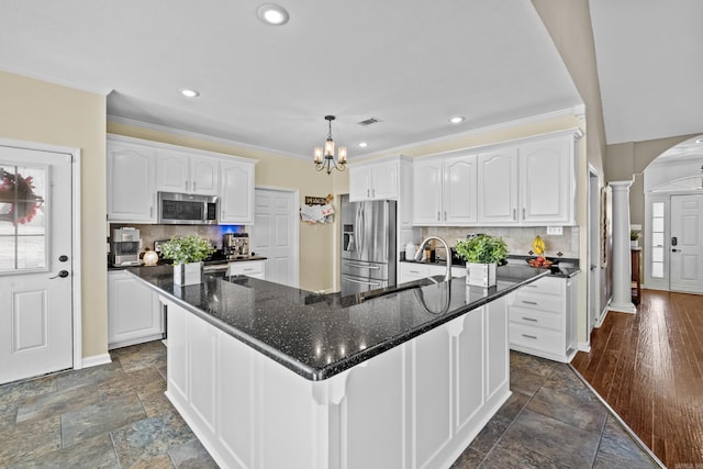 kitchen with stone tile floors, arched walkways, a sink, stainless steel appliances, and white cabinets