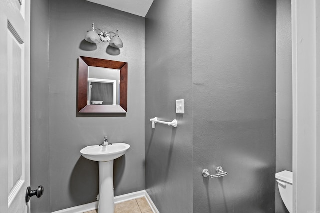 half bathroom featuring baseboards, a sink, tile patterned floors, toilet, and a textured wall