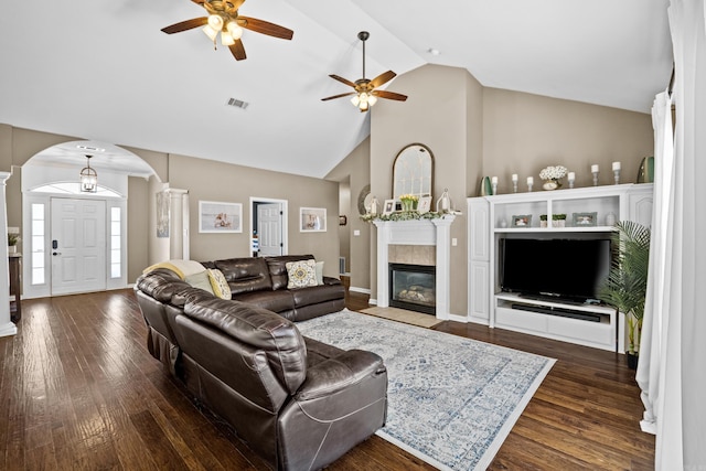 living room featuring visible vents, high vaulted ceiling, a tiled fireplace, dark wood finished floors, and arched walkways