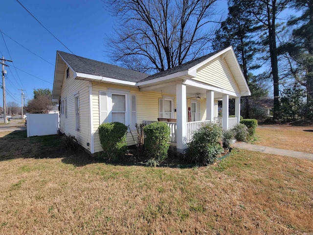 view of side of home with a yard, roof with shingles, and a porch