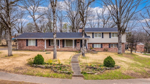 split level home featuring a front lawn, brick siding, and a chimney