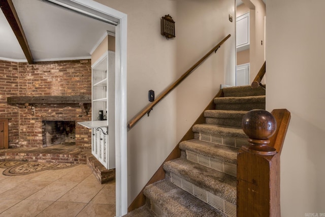 staircase with beamed ceiling, ornamental molding, a fireplace, and tile patterned flooring