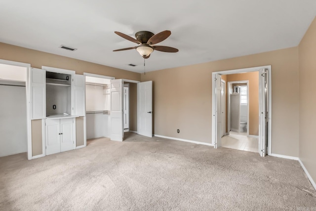 unfurnished bedroom featuring visible vents, baseboards, ceiling fan, light colored carpet, and two closets