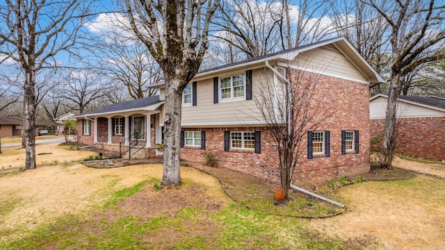 split level home featuring brick siding, a porch, and a front yard