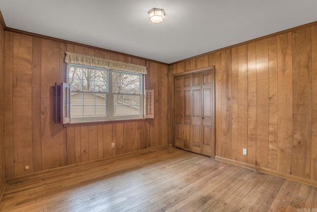 unfurnished bedroom with a closet, wooden walls, baseboards, and wood-type flooring