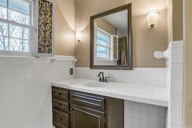 bathroom featuring a wealth of natural light, a wainscoted wall, vanity, and tile walls