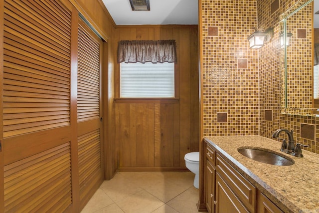 bathroom with toilet, tasteful backsplash, wood walls, tile patterned flooring, and vanity