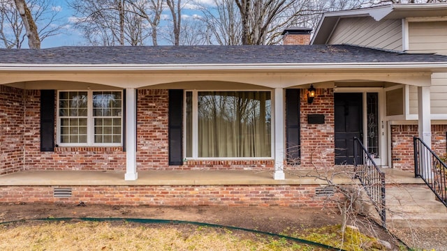 doorway to property with crawl space, covered porch, a chimney, and brick siding