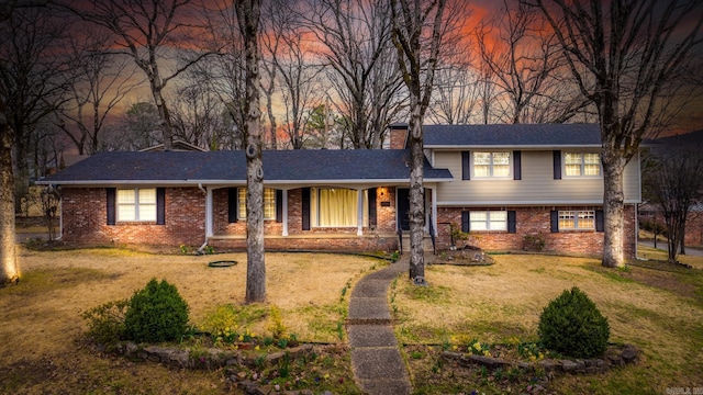 split level home featuring brick siding, a chimney, and a front lawn