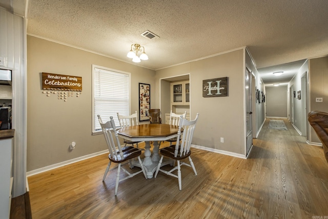 dining area with visible vents, ornamental molding, a textured ceiling, and wood finished floors