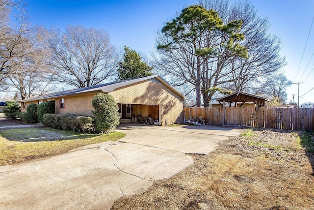 view of side of property featuring brick siding, driveway, a gazebo, and fence