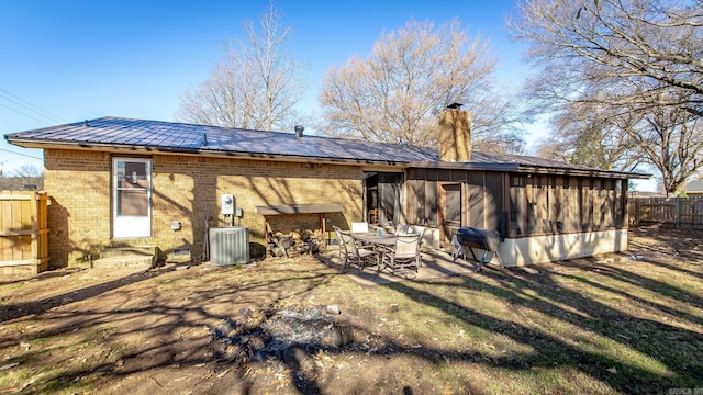 rear view of house featuring fence, metal roof, brick siding, central AC unit, and a chimney