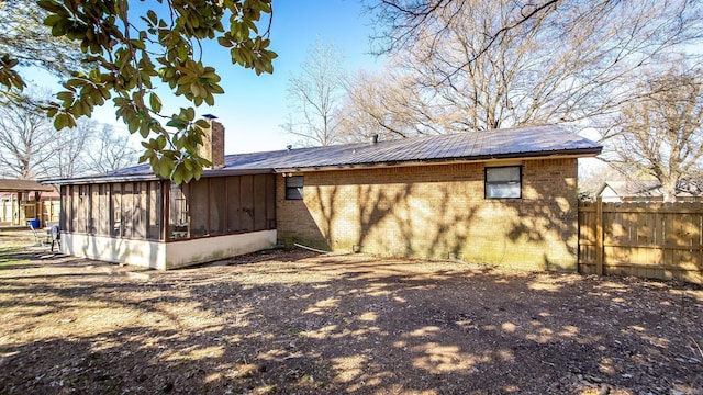 view of side of property featuring fence, a sunroom, metal roof, brick siding, and a chimney