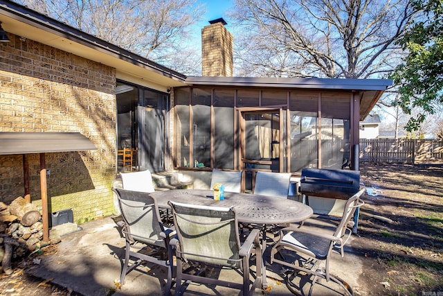 view of patio featuring outdoor dining space, a grill, fence, and a sunroom