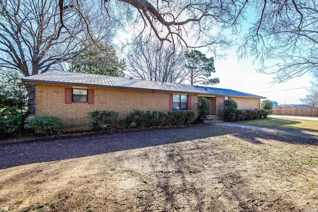 ranch-style home with fence, brick siding, dirt driveway, and metal roof