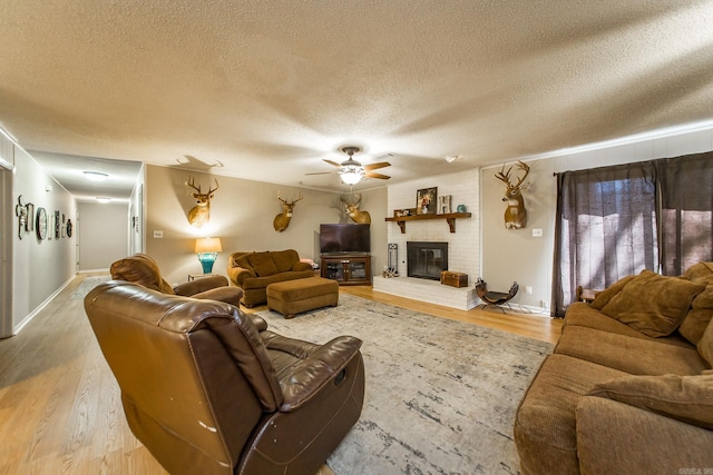 living room featuring wood finished floors, baseboards, a ceiling fan, a fireplace, and a textured ceiling