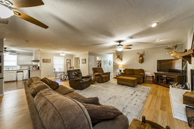 living room with light wood-style flooring, a fireplace, a textured ceiling, and ceiling fan