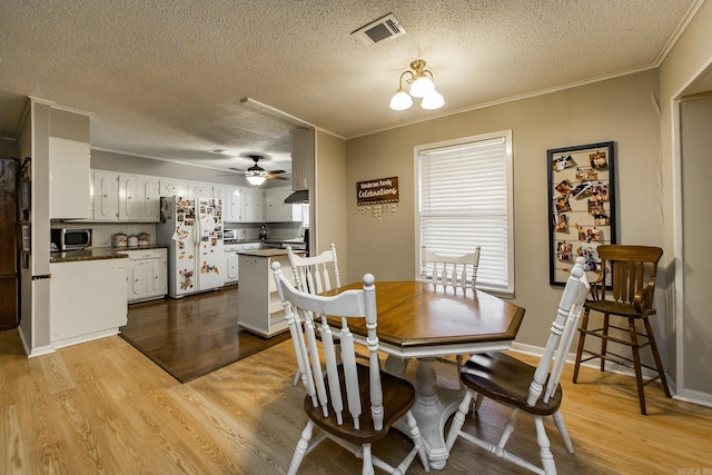 dining room with visible vents, light wood-style flooring, crown molding, and a ceiling fan