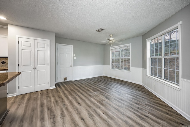 unfurnished dining area with ceiling fan, a wainscoted wall, a textured ceiling, and dark wood-style floors