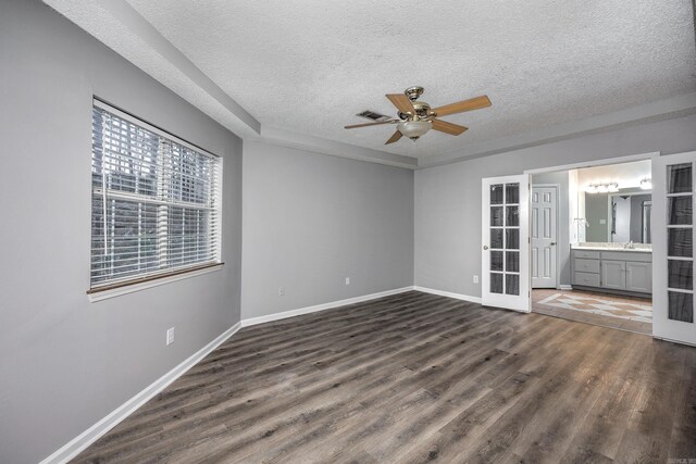 empty room with visible vents, a textured ceiling, dark wood finished floors, baseboards, and ceiling fan