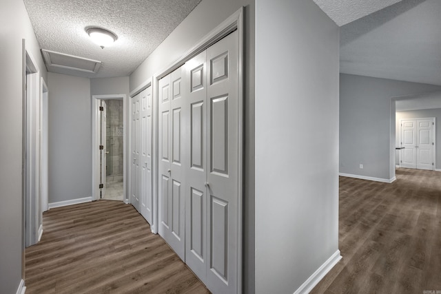 corridor featuring a textured ceiling, baseboards, attic access, dark wood-style flooring, and vaulted ceiling