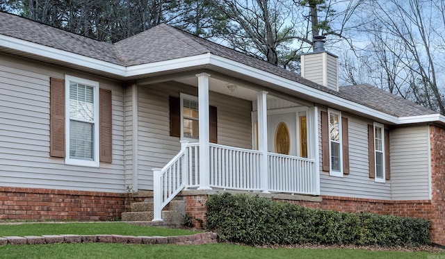 doorway to property with brick siding, a porch, a chimney, and a shingled roof