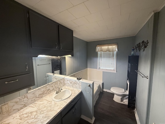 bathroom with baseboards, toilet, a garden tub, wood finished floors, and vanity