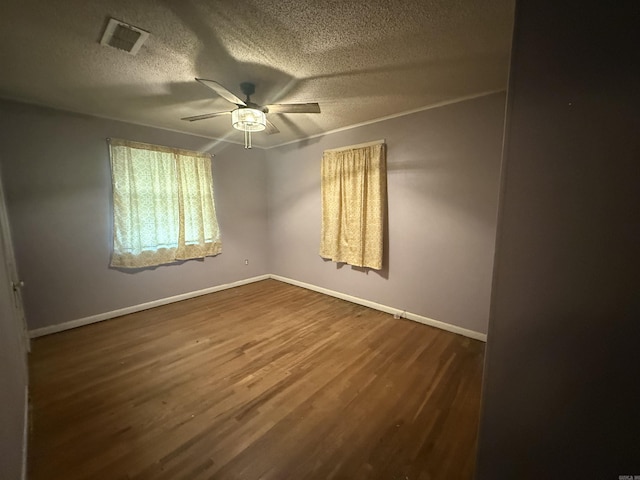 unfurnished room featuring dark wood-style floors, baseboards, visible vents, ceiling fan, and a textured ceiling