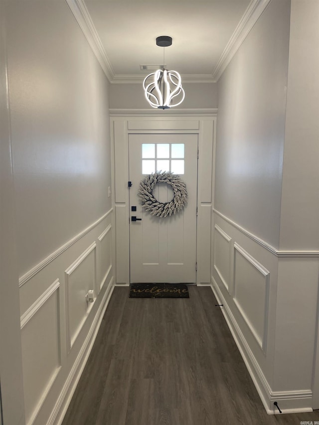 doorway to outside with dark wood finished floors, a notable chandelier, a decorative wall, and ornamental molding