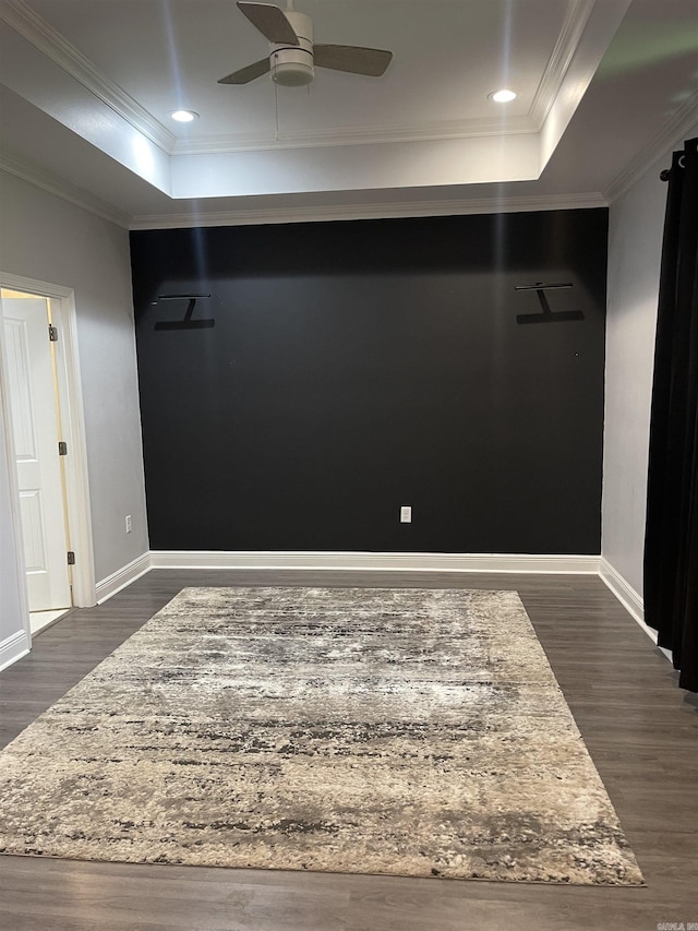 spare room featuring a tray ceiling, dark wood-type flooring, ornamental molding, and a ceiling fan