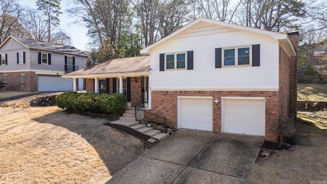 split level home with brick siding, an attached garage, covered porch, a chimney, and driveway