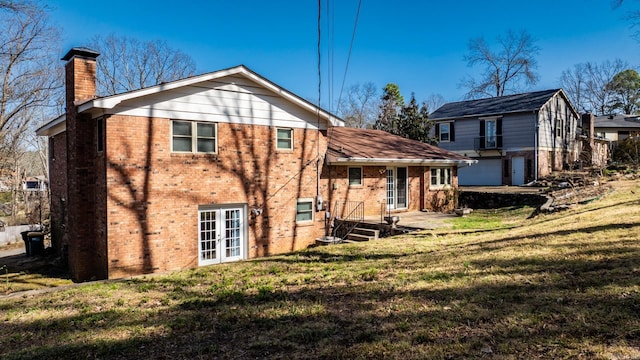 back of house with a yard, french doors, brick siding, and a chimney