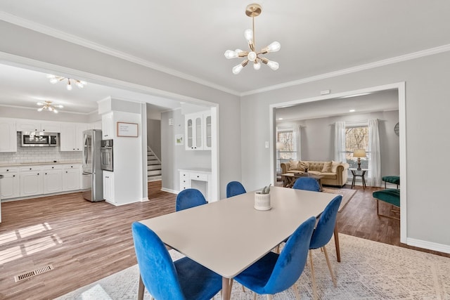 dining area featuring an inviting chandelier, light wood-style floors, visible vents, and ornamental molding