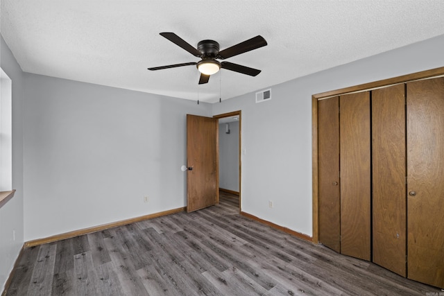 unfurnished bedroom featuring visible vents, baseboards, wood finished floors, a closet, and a textured ceiling