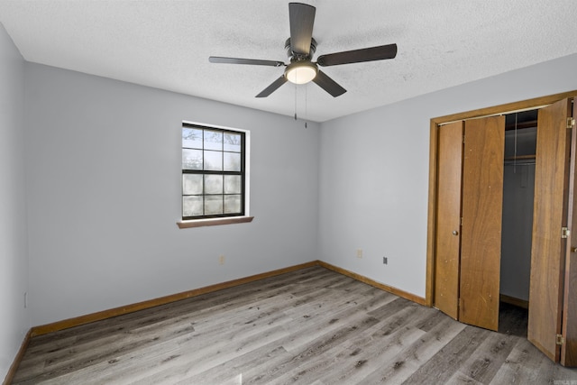 unfurnished bedroom featuring a closet, a textured ceiling, baseboards, and wood finished floors