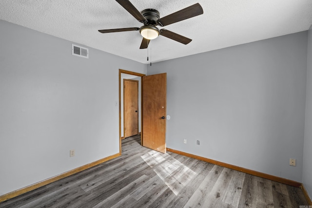 unfurnished room with visible vents, baseboards, wood finished floors, a textured ceiling, and a ceiling fan