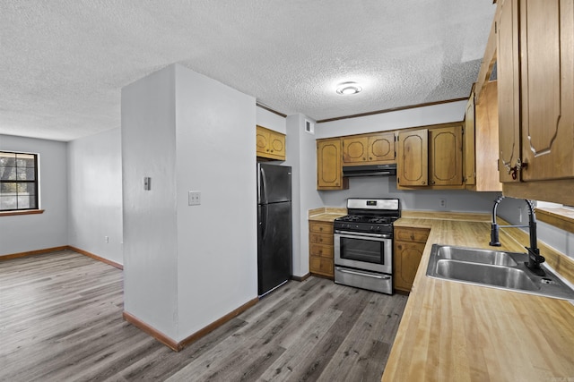 kitchen featuring under cabinet range hood, freestanding refrigerator, wood finished floors, gas stove, and a sink