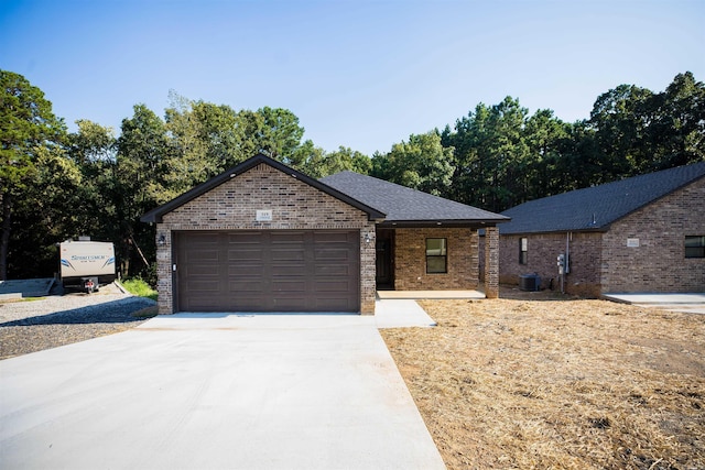 single story home with brick siding, an attached garage, a shingled roof, central AC, and driveway