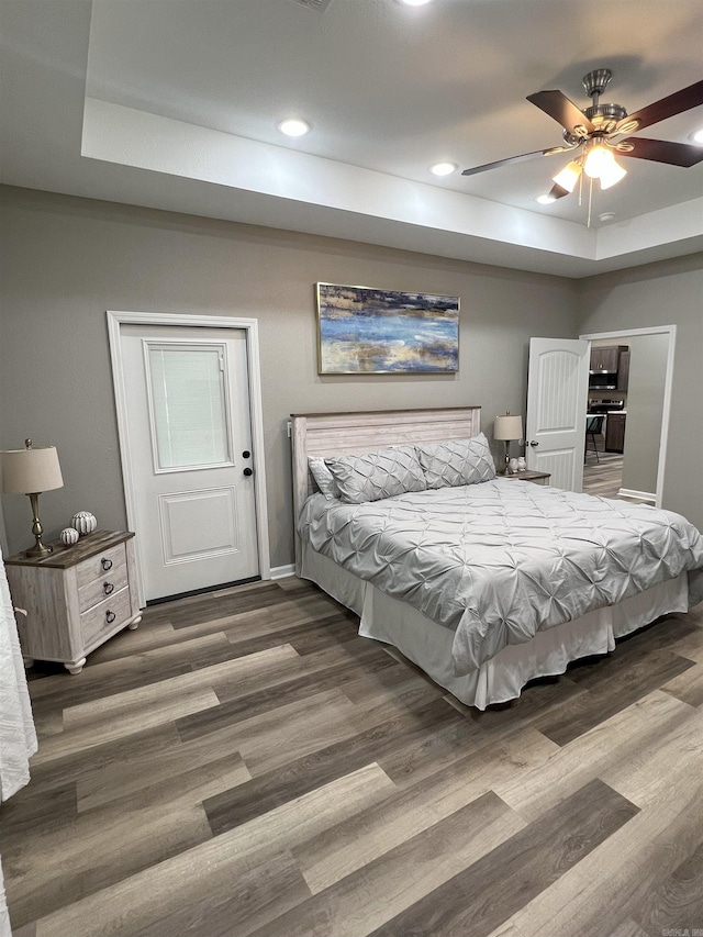 bedroom featuring wood finished floors, baseboards, a tray ceiling, recessed lighting, and ceiling fan